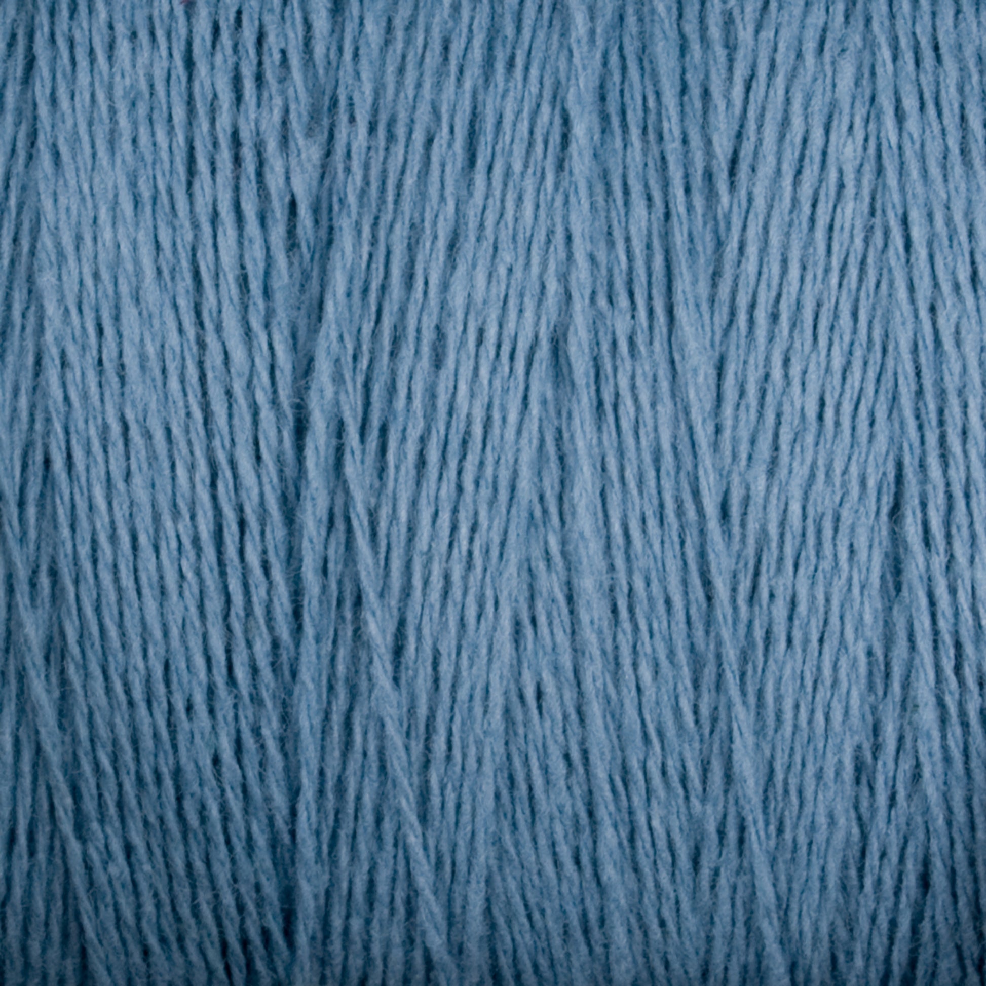 Close-up image of the soft, light blue Homestead 8/2 Cotton Yarn on a mini-cone by Supreme Corp. The fibers appear smooth and polished, with visible strands running vertically, suggesting a tightly wound skein of versatile yarns ready for knitting or other textile crafts.