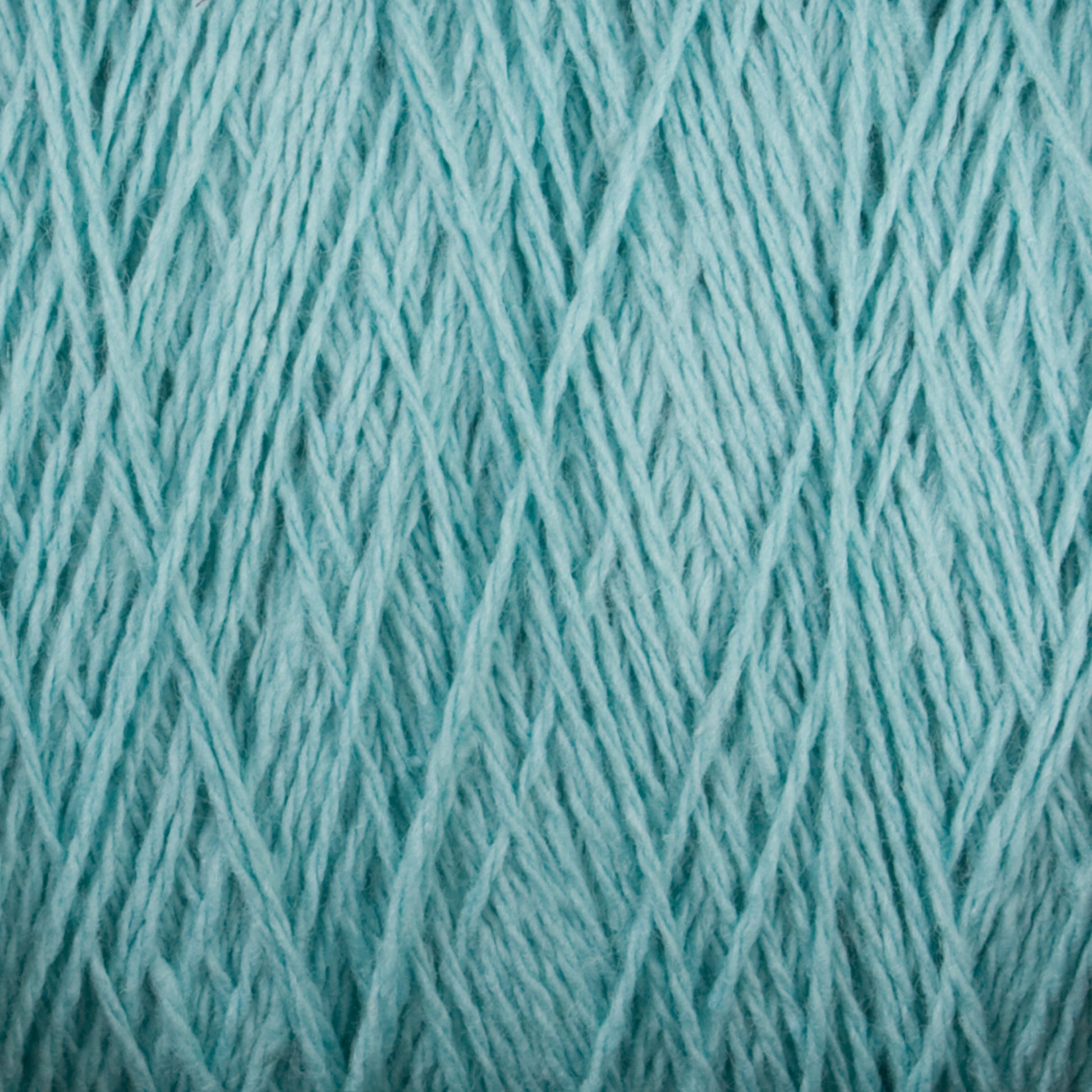 Close-up image of Homestead 8/2 Cotton Yarn | Mini-cone in light blue from Supreme Corp, tightly wound into a ball. The strands of this versatile yarn create a textured and intricate pattern of intertwining fibers across the entire frame. The overall appearance is soft and detailed.