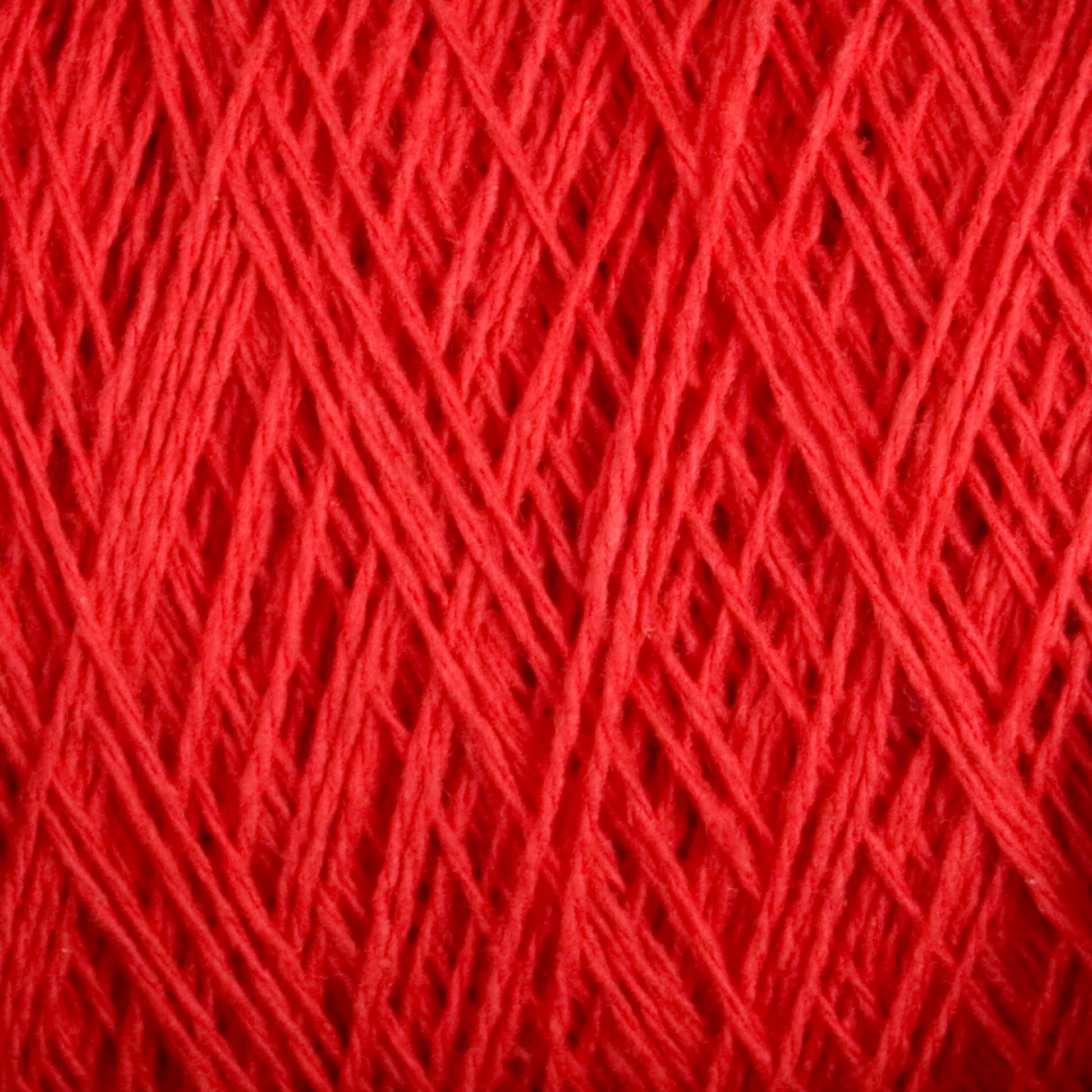 Close-up image showing the intricate and detailed texture of tightly wound Homestead 8/2 Cotton Yarn | Large Cone from Supreme Corp. The fibers of this machine-washable yarn are arranged in a crisscross pattern, highlighting the different shades and thicknesses of the red strands.