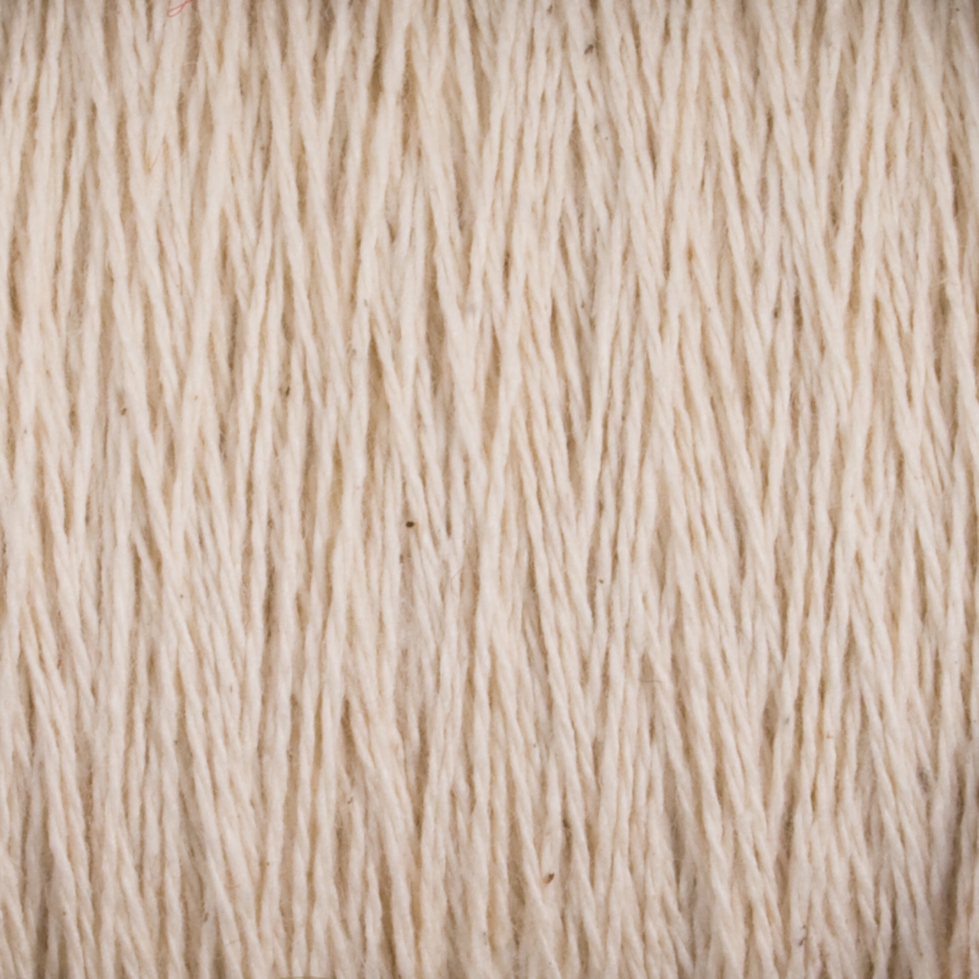 A close-up image of Homestead 8/2 Cotton Yarn | Mini-cone by Supreme Corp, showcasing tightly wound beige fibers running vertically. The texture appears rough, with strands slightly uneven, creating a natural, rustic look reminiscent of versatile yarns.