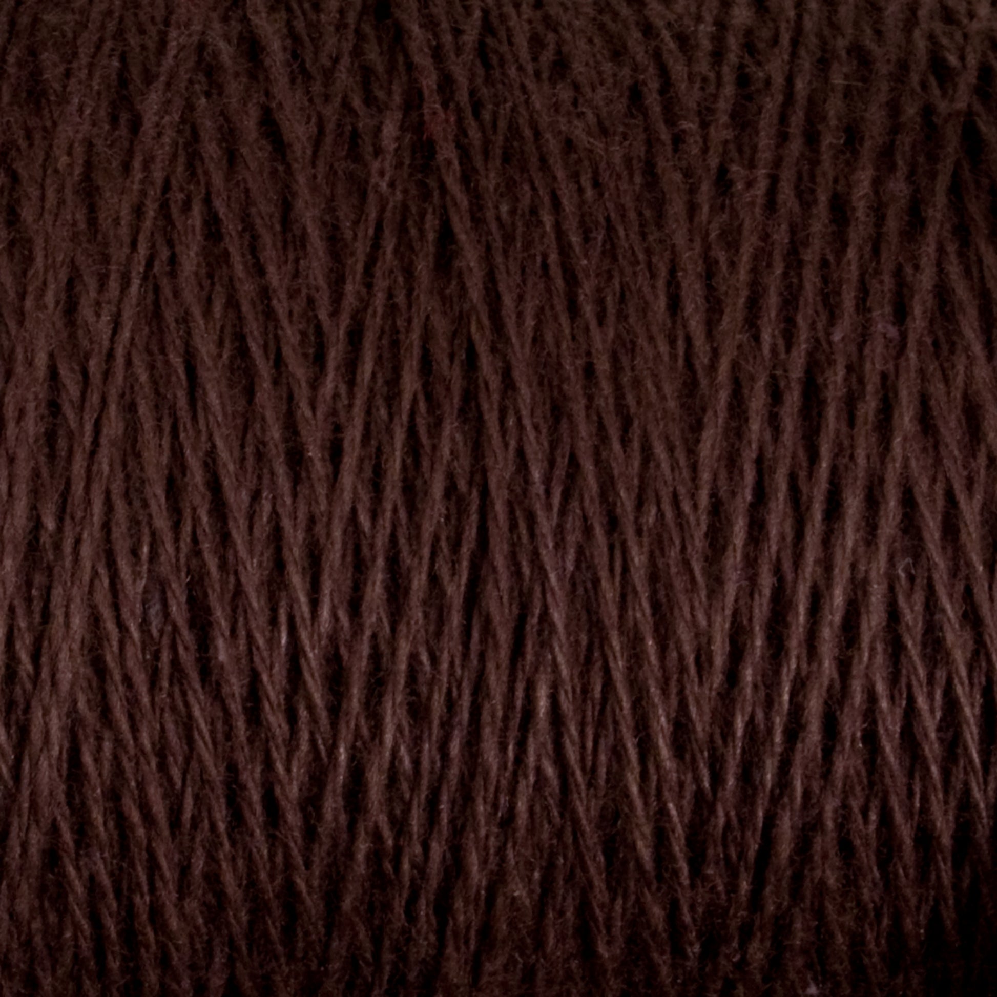 A close-up image of a spool of Supreme Corp's Homestead 8/2 Cotton Yarn in dark brown, showcasing the intricate texture of the fibers wound around the mini-cone. The intertwined threads form a pattern of diagonal lines, with subtle variations in tone and texture, demonstrating how this weaving yarn can be both functional and beautiful.