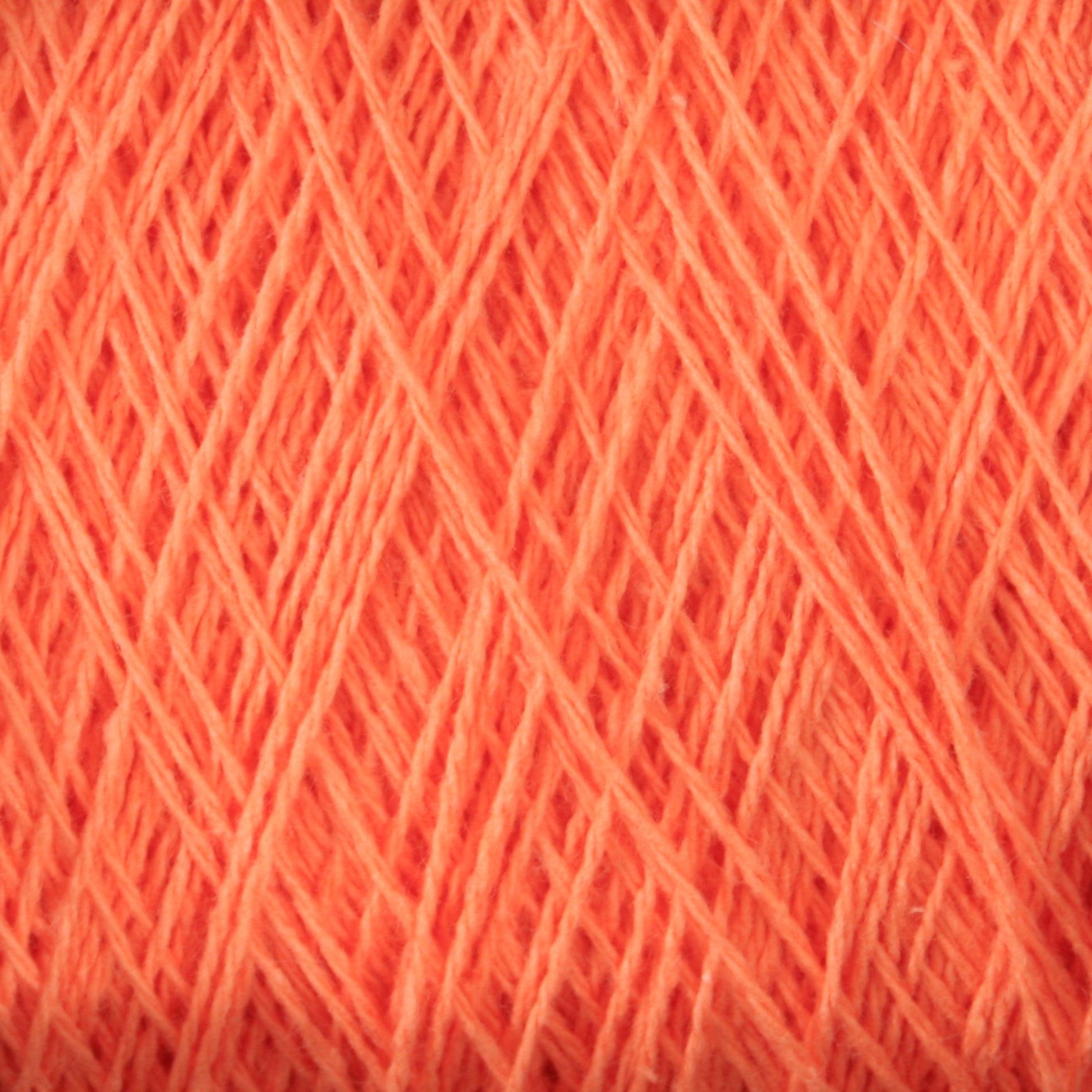 Close-up image of a tightly wound ball of coral-colored, versatile yarn. The thin strands of Homestead 8/2 Cotton Yarn from Supreme Corp are densely packed, creating a textured pattern of intersecting lines and subtle shadows, perfect for weaving projects.