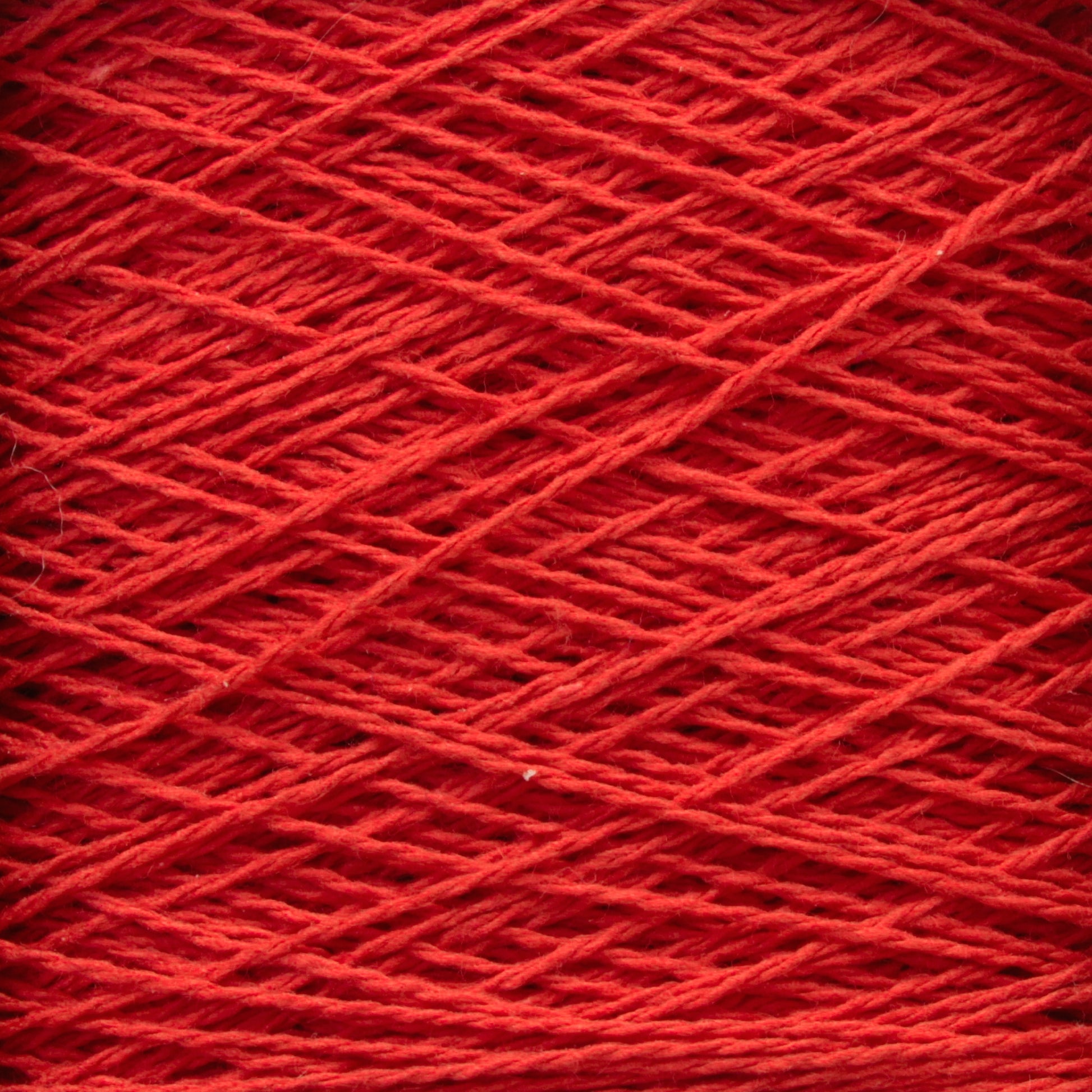 A close-up image of red Homestead 8/2 Cotton Yarn | Large Cone by Supreme Corp wound around itself, creating a textured and crisscrossing pattern. The machine-washable strands are tightly coiled, showcasing the fiber's intricate and uniform arrangement.