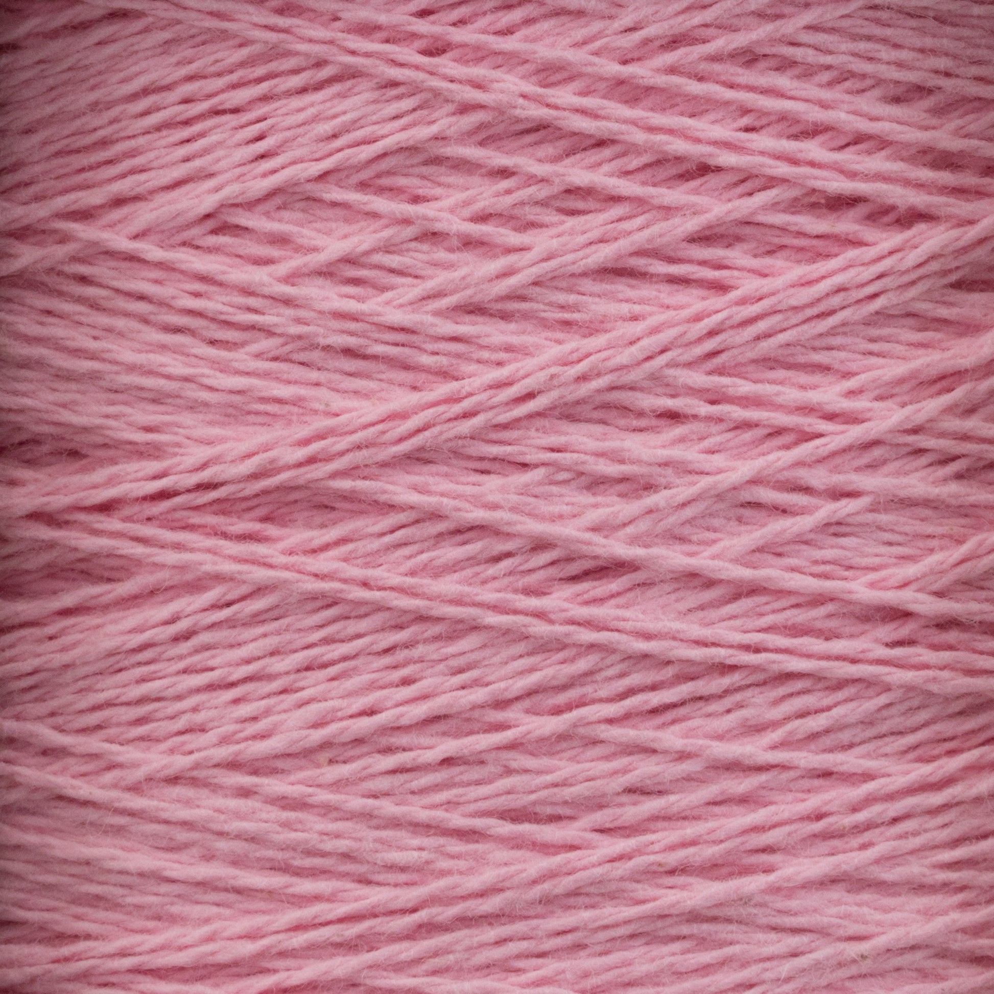 Close-up image of light pink Homestead 8/2 Cotton Yarn | Large Cone by Supreme Corp, showcasing its soft texture and intricately wound strands. The yarn features a subtle sheen, with fibers running at varying angles, highlighting the layers and depth of this machine-washable material.