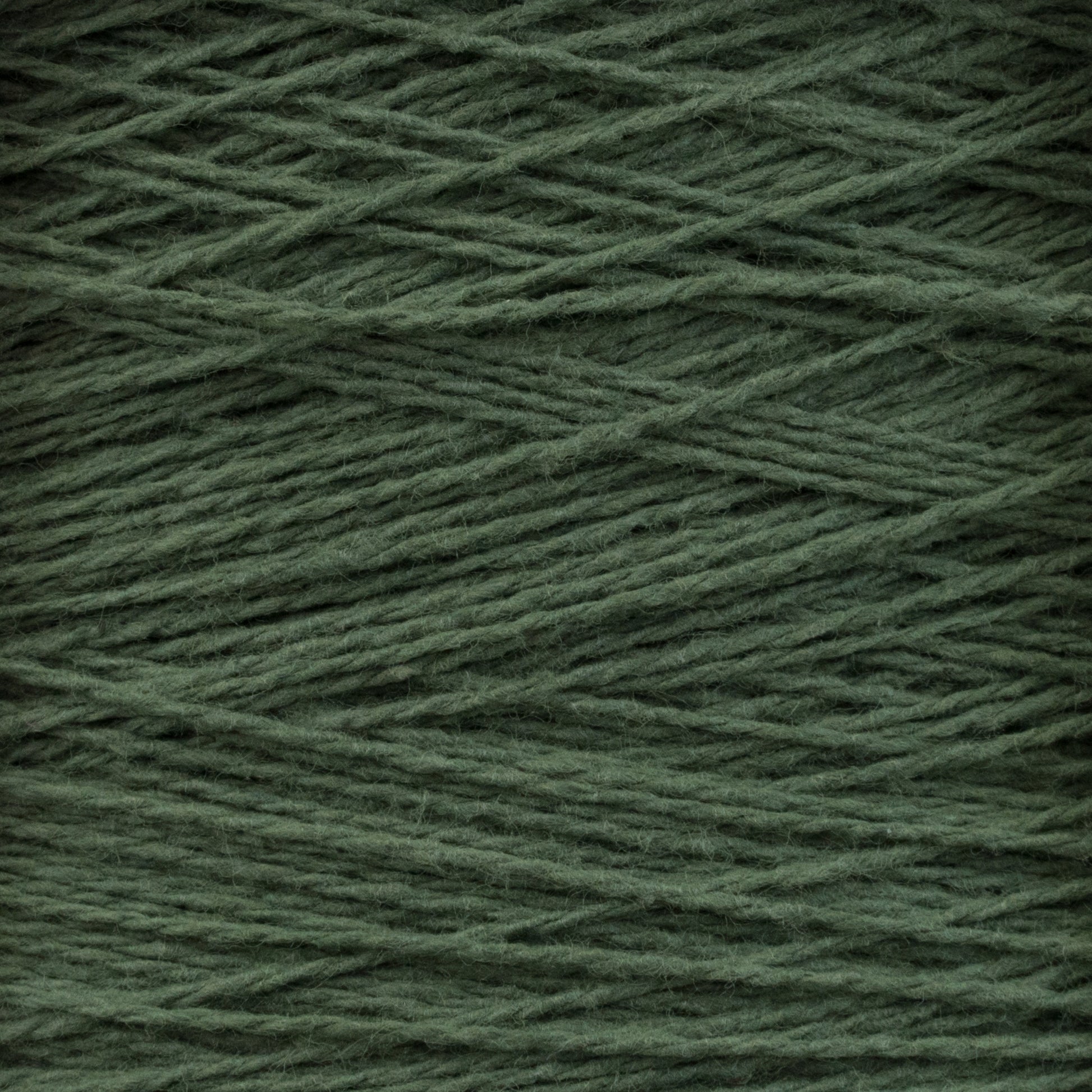 Close-up of a spool of Homestead 8/2 Cotton Yarn | Mini-cone by Supreme Corp. The dark green, machine-washable strands are tightly wound and have a slightly fuzzy texture. The image highlights the interlacing threads and fibrous details of this versatile yarn, perfect for various weaving projects.