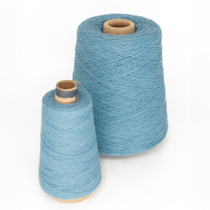 Two mini-cones of light blue, versatile yarn from Supreme Corp's Homestead 8/2 Cotton Yarn collection are displayed against a white background. The machine-washable yarn is neatly wrapped around the mini-cones, with the larger cone positioned slightly behind and to the left of the smaller one. Both cones have cardboard cores.