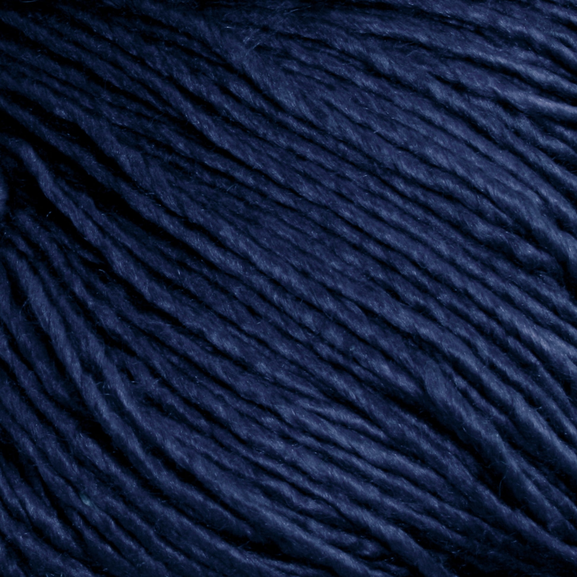 Close-up image of Halcyon Yarn's Gemstone Soft Twist Silk Yarn in dark blue, tightly wound together and showcasing the texture and fiber details. The yarn appears smooth and slightly glossy, with subtle variations in color depth that highlight a rich, deep blue shade reminiscent of gemstone silks.