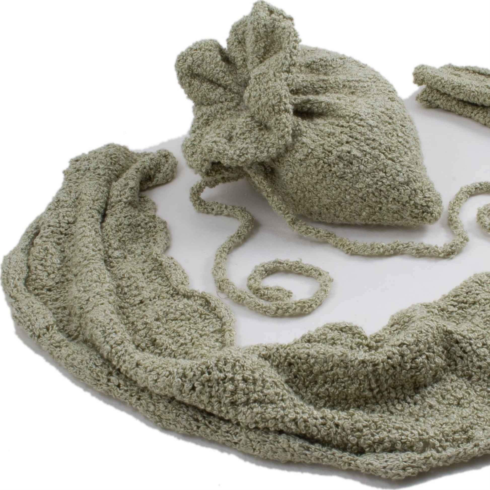 An intricately knitted, sage-green baby blanket is spread out. Made from Silk Boucle Yarn by Halcyon Yarn, it features a scalloped edge and is accompanied by a matching drawstring bag. The soft, textured fabric is neatly displayed on a white background—an epitome of luxury accessories for your little one.