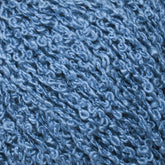 Close-up image of Halcyon Yarn’s Gemstone Silk Bouclé showing the blue textured yarn with a curly appearance. The yarn features a shiny, almost reflective quality and tightly looped fibers, giving it a richly textured and soft look. The vibrant, uniform blue color is reminiscent of gemstone silks.