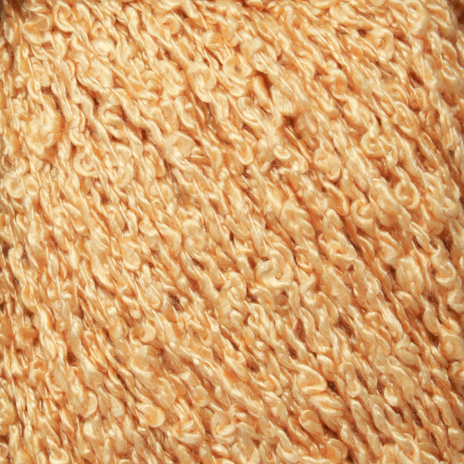 A close-up of the Gemstone Silk Bouclé by Halcyon Yarn showcases a tightly woven, curly, and soft material in a golden tan color. The texture is reminiscent of silk bouclé or wool with a slightly shiny finish.