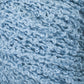 Close-up view of Gemstone Silk Bouclé in light blue, featuring a textured yarn with a curly, bouclé appearance. This Halcyon Yarn has a soft and fluffy texture, showcasing its intricate loops and twists.