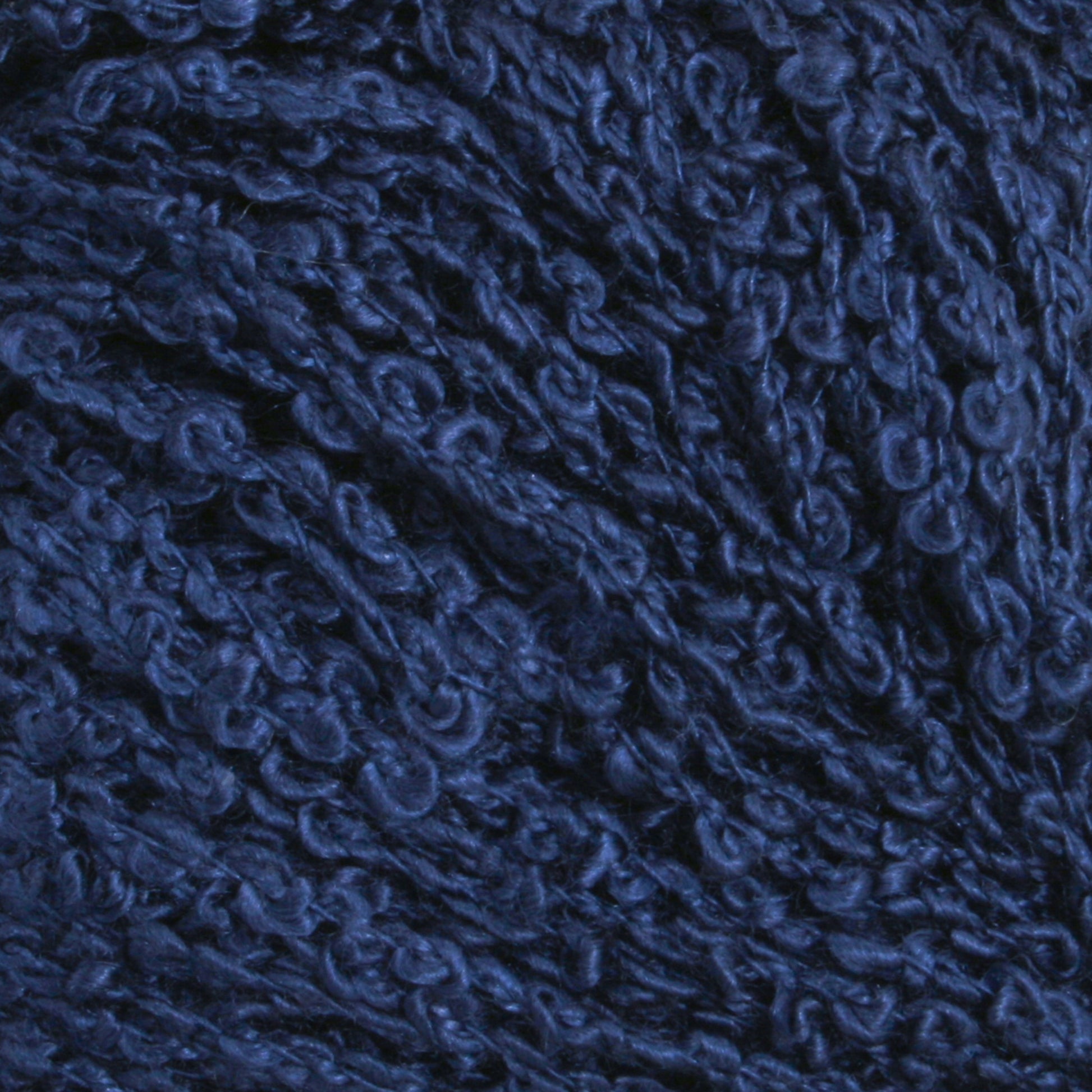 A close-up image of dark blue yarn with a textured, Silk Bouclé appearance. The tightly twisted fibers of the Gemstone Silk Bouclé from Halcyon Yarn give it a dense and rich look.