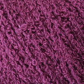 A close-up image of textured, purple yarn with a boucle pattern, perfect for knitting and weaving. The yarn appears soft and slightly fuzzy, with tiny loops and twists creating a rich, tactile surface. Named Gemstone Silk Bouclé by Halcyon Yarn, the deep shade of purple resembles luxurious silk yarn in its richness.