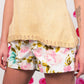 Person modeling a cream-colored Celosia Camisole from Twist Collective paired with floral-printed shorts. Their left arm displays an abstract tattoo. The background features a pattern of large pink polka dots.