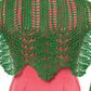 A person wearing a pink dress is seen from the back, showcasing an Unnathi Shawl by Twist Collective, adorned with vibrant green lace patterns. The intricately crocheted shawl drapes elegantly over the shoulders and upper back, displaying a symmetrical design finished with an i-cord bind-off. (Credit: Cristy Johns).