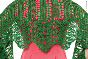 A person wearing a pink dress is seen from the back, showcasing an Unnathi Shawl by Twist Collective, adorned with vibrant green lace patterns. The intricately crocheted shawl drapes elegantly over the shoulders and upper back, displaying a symmetrical design finished with an i-cord bind-off. (Credit: Cristy Johns).