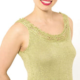 A person wearing the Papeda Camisole Pattern by Twist Collective, featuring a light green sleeveless knitted design with intricate lace yoke detailing around the neckline and armholes, smiles against a plain white background.