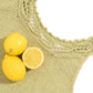 A close-up of a knitted green Papeda Camisole by Twist Collective with a decorative lace yoke. Three lemons rest on top of the camisole, one of which is halved to reveal its insides. The background is white, and © Cristy Johns is visible in the image.