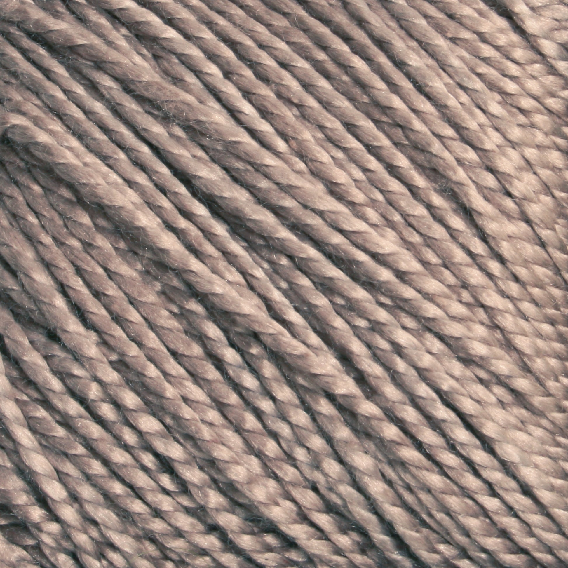 Close-up of beige Gemstone Silk 2/5 yarns from Halcyon Yarn showing twisted fibers and a textured surface, suggesting a soft and smooth material. The strands are uniformly coiled and densely packed, indicating a high-quality, tightly spun yarn.