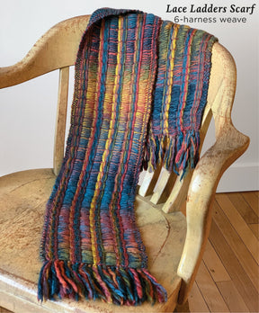 A colorful, warm woven scarf from Halcyon Yarn with a lace ladders pattern, created using a 6-harness weave and soft bulky weight yarn, is draped over a rustic wooden chair. The Lace Ladders Woven Scarf features vibrant hues including blue, red, yellow, and green, with fringed ends. Text on the image reads "Lace Ladders Woven Scarf by Halcyon Yarn - 6-harness weave.