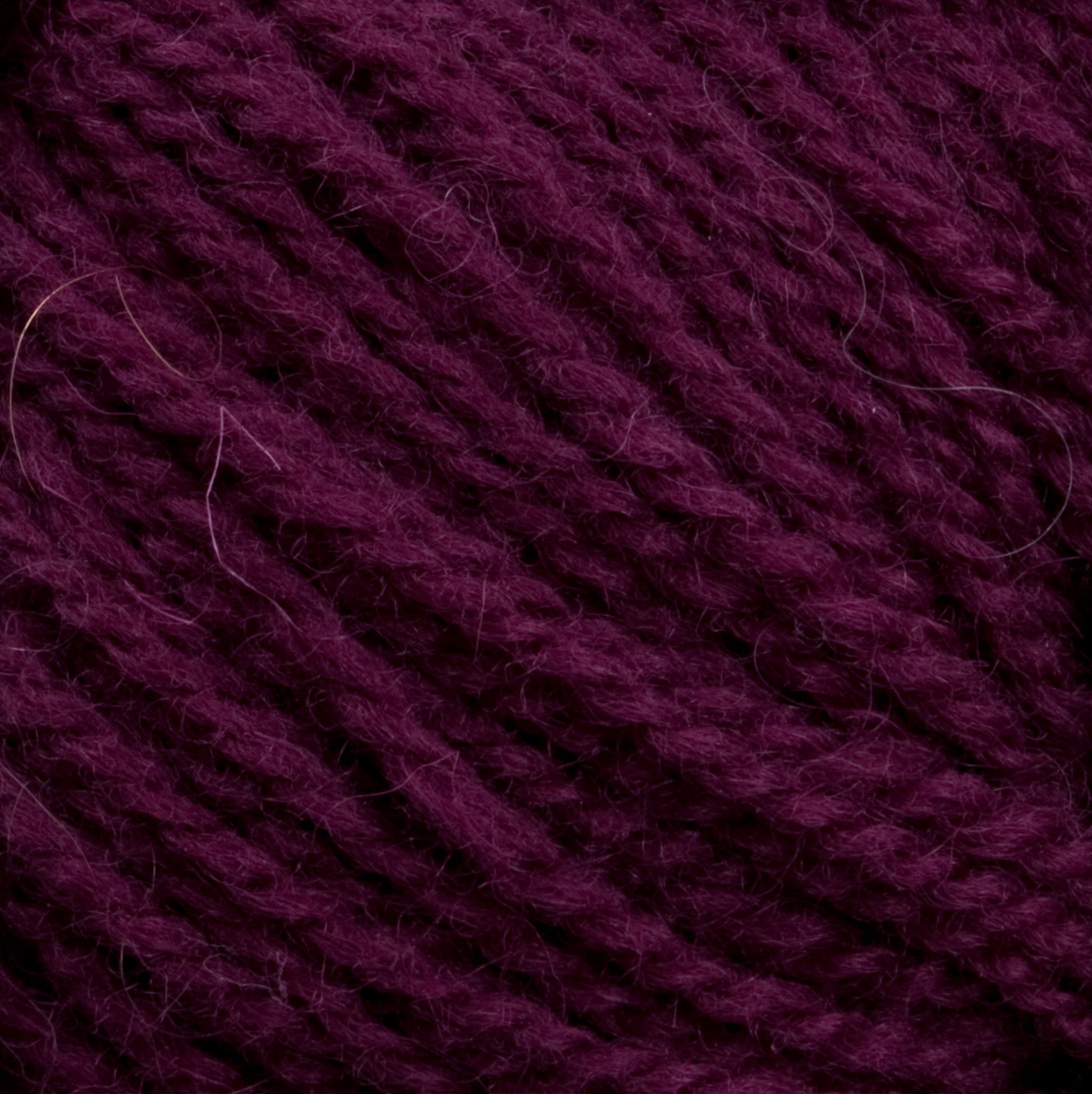 Close-up of a ball of dark purple Victorian 2-Ply Wool Yarn by Halcyon Yarn, showing its soft, textured strands coiled together tightly, with a few stray fibers visible. Perfect for hand knitting projects, this sport weight wool promises both comfort and durability.