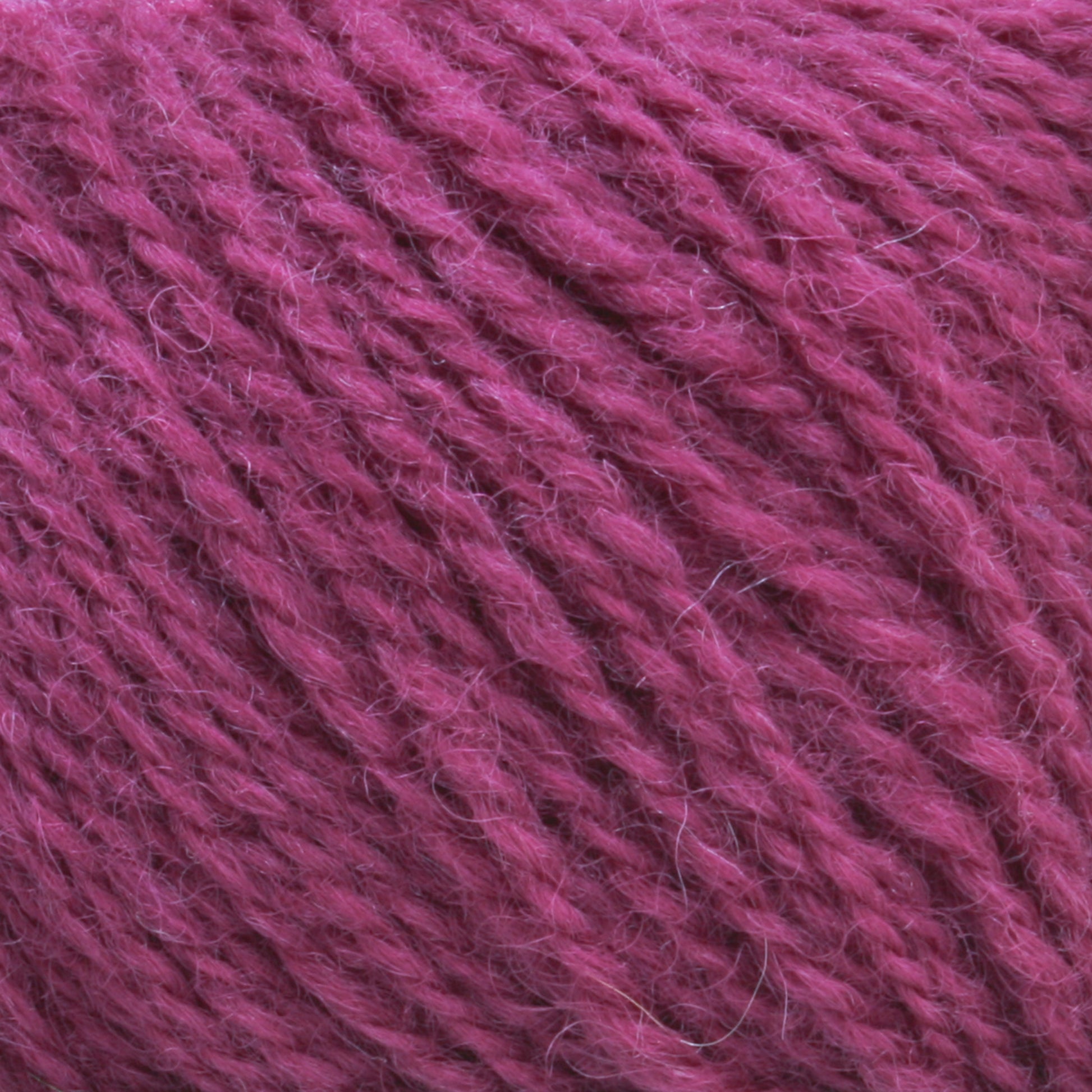 Close-up image of a ball of Halcyon Yarn's Victorian 2-Ply Wool Yarn in magenta, showcasing its soft and fuzzy texture. The Sport weight yarn is tightly wound, revealing detailed fibrous strands and gentle color variations, making it perfect for hand knitting.