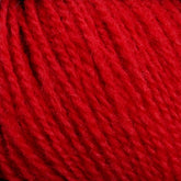 Close-up image of bright red, Victorian 2-Ply Wool Yarn by Halcyon Yarn shows its tightly twisted fibers and soft, plush texture, suitable for knitting or crocheting. The image highlights the sport weight yarn's vibrant color and detailed texture, emphasizing its quality and tactile appearance for hand knitting.