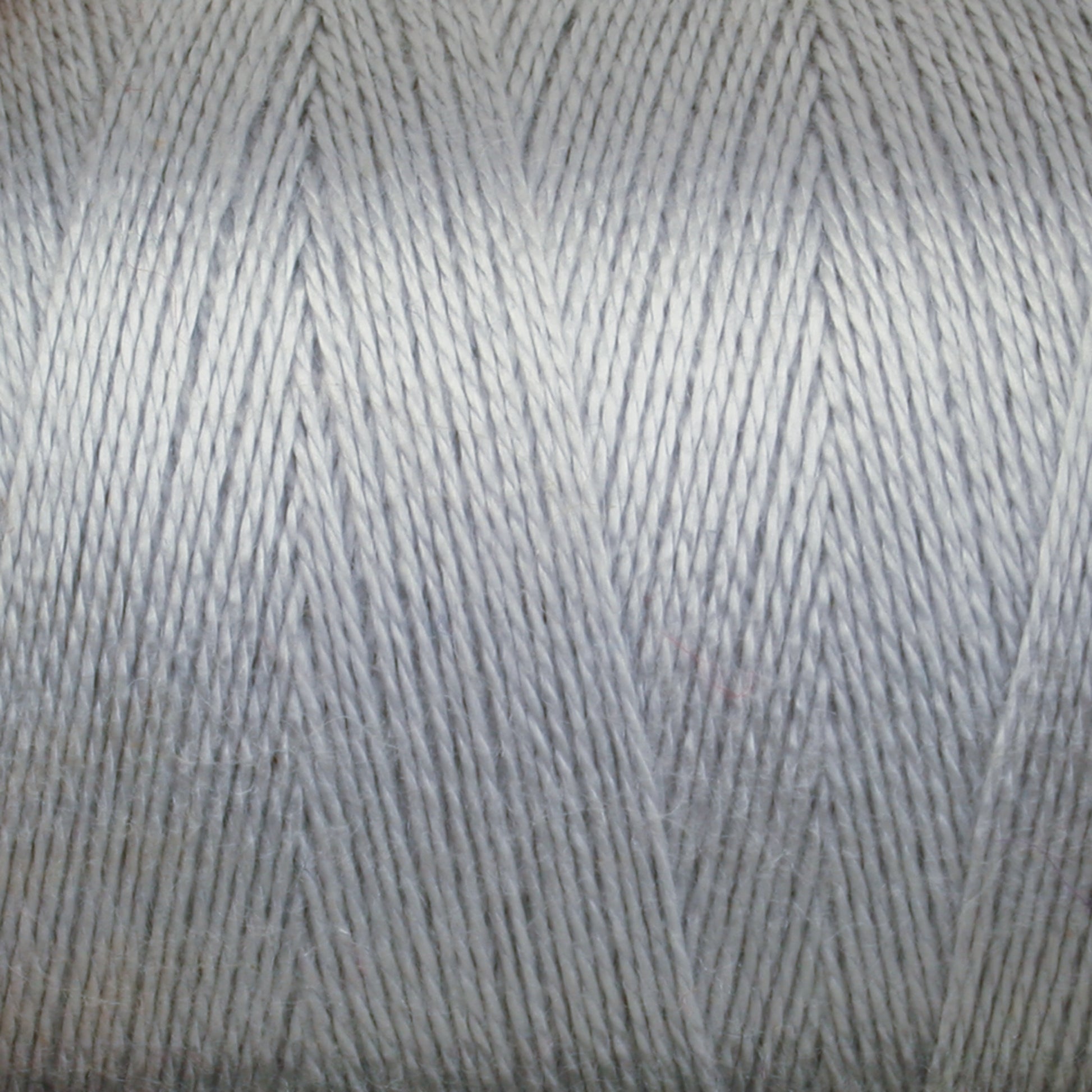 Close-up image of a spool of light gray 8/2 Tencel Yarn from Maurice Brassard. The tightly woven, thin threads create a smooth texture. The surface showcases a uniform, slightly shiny appearance, perfect for weaving projects and knitting accessories, highlighting the fine details of the individual strands.