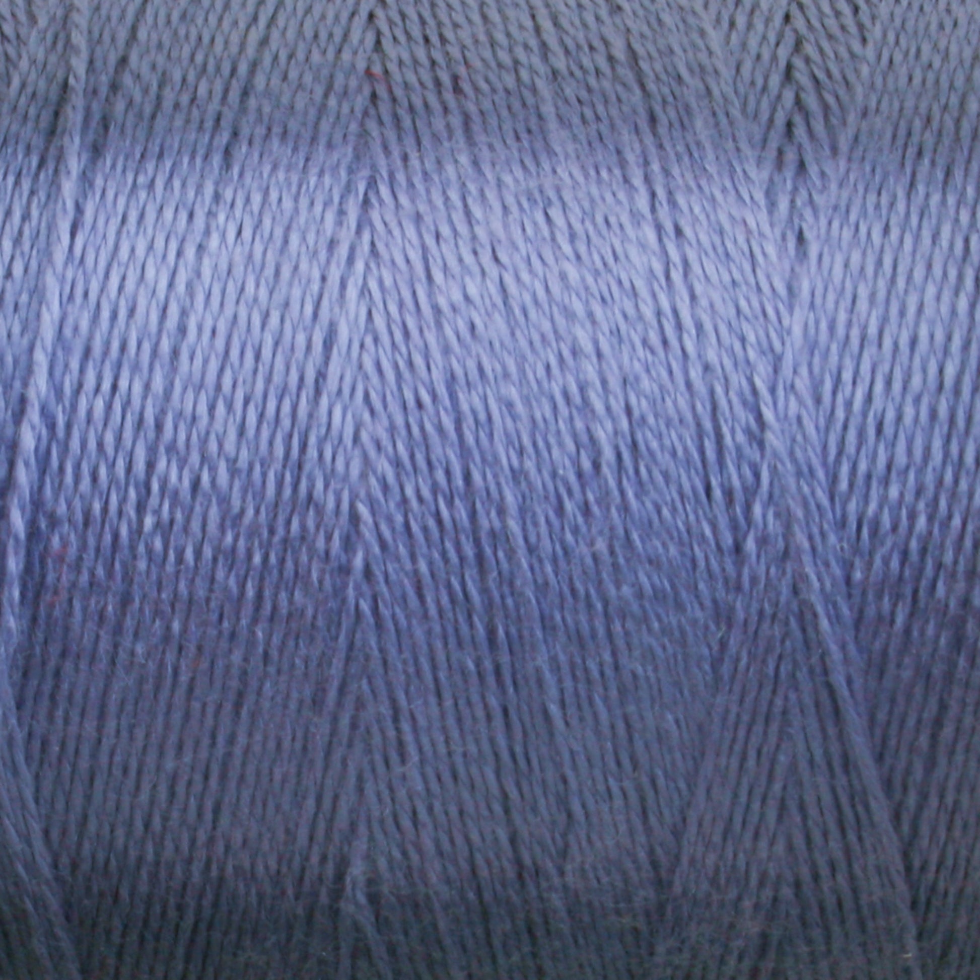 Close-up image of a spool of Maurice Brassard's 8/2 Tencel Yarn in blue. The tightly wound thread creates a textured, diagonal pattern, showcasing the smooth, shiny surface. The color is a mid-tone blue with subtle variations in light reflecting off the material, perfect for knitting accessories or weaving projects.