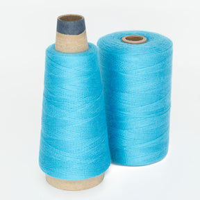 Two spools of Maurice Brassard's 8/2 Tencel Yarn in bright blue are displayed against a white background. One spool is a mini cone, while the other spool is cylindrical and more compact. Both spools have a cardboard center and are tightly wound with the blue thread, making them perfect for knitting accessories or weaving projects.