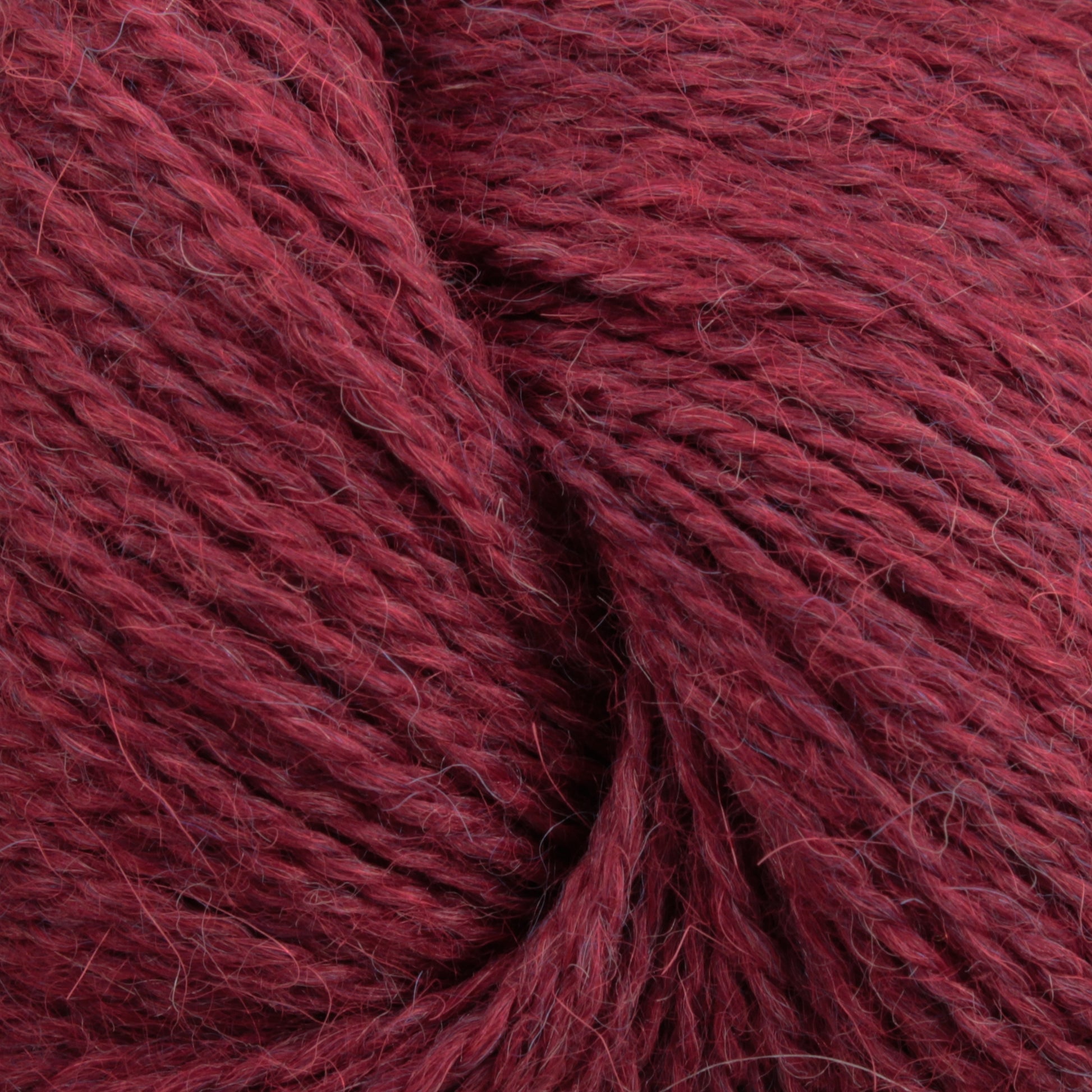 A close-up image of soft, deep red yarn fibers. The texture appears slightly fuzzy, with individual strands visible. Made from Baby alpaca, the Herriot Fine Alpaca by Juniper Moon Farm yarn is tightly wound, creating a cozy and warm appearance ideal for knitting sumptuous socks. This premium product is offered by Knitting Fever / Euro.