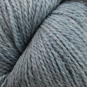 Close-up image of soft, thick grayish-blue Herriot Fine Alpaca yarn by Juniper Moon Farm twisted into a skein, showing the texture and individual fibers of the material. The yarn appears slightly fluffy, indicating a cozy, warm feel perfect for sumptuous socks. This luxurious product is brought to you by Knitting Fever / Euro.