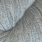 Close-up of a skein of light gray Herriot Fine Alpaca yarn by Juniper Moon Farm, with a soft and slightly fuzzy texture, wrapped in a circular fashion. The yarn fibers from Knitting Fever / Euro are discernible, creating a detailed view of its texture, perfect for crafting sumptuous socks.