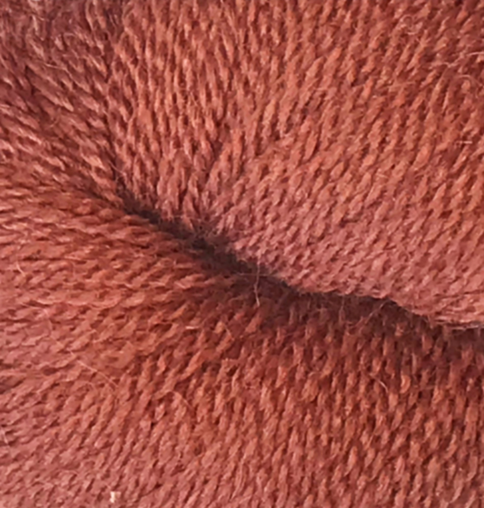 Close-up of a skein of Herriot Fine Alpaca by Juniper Moon Farm from Knitting Fever / Euro, showcasing its tightly woven fibers and soft texture. The reddish-brown yarn appears to be thickly twisted, indicating a durable and cozy material suitable for knitting sumptuous socks or lightweight accessories.