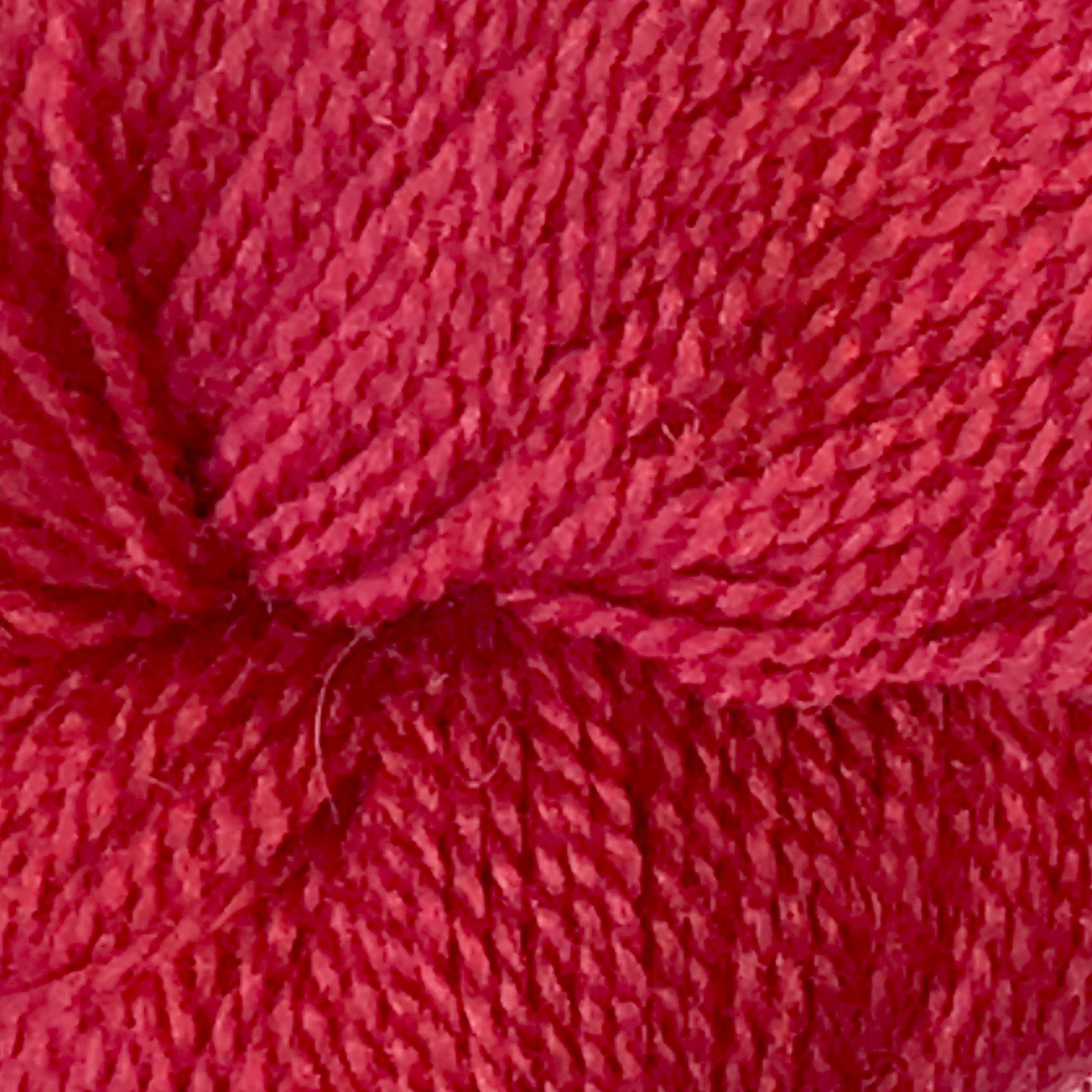 Close-up view of Herriot Fine Alpaca by Juniper Moon Farm yarn, showing detailed texture and tightly wound strands. The vibrant red fibers are densely packed, with visible twists and loops, indicating a soft yet durable material perfect for knitting sumptuous socks or lightweight accessories. Brought to you by Knitting Fever / Euro.