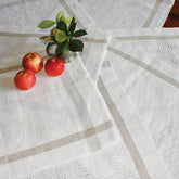 A white linen table runner with a subtle checkered pattern, crafted from Newport Linen, is spread on a wooden table. Three red apples and a small glass jar with green leafy plants decorate the table, while Classic Linen Newport Towels by Halcyon Yarn lie underneath, adding texture to the setting.