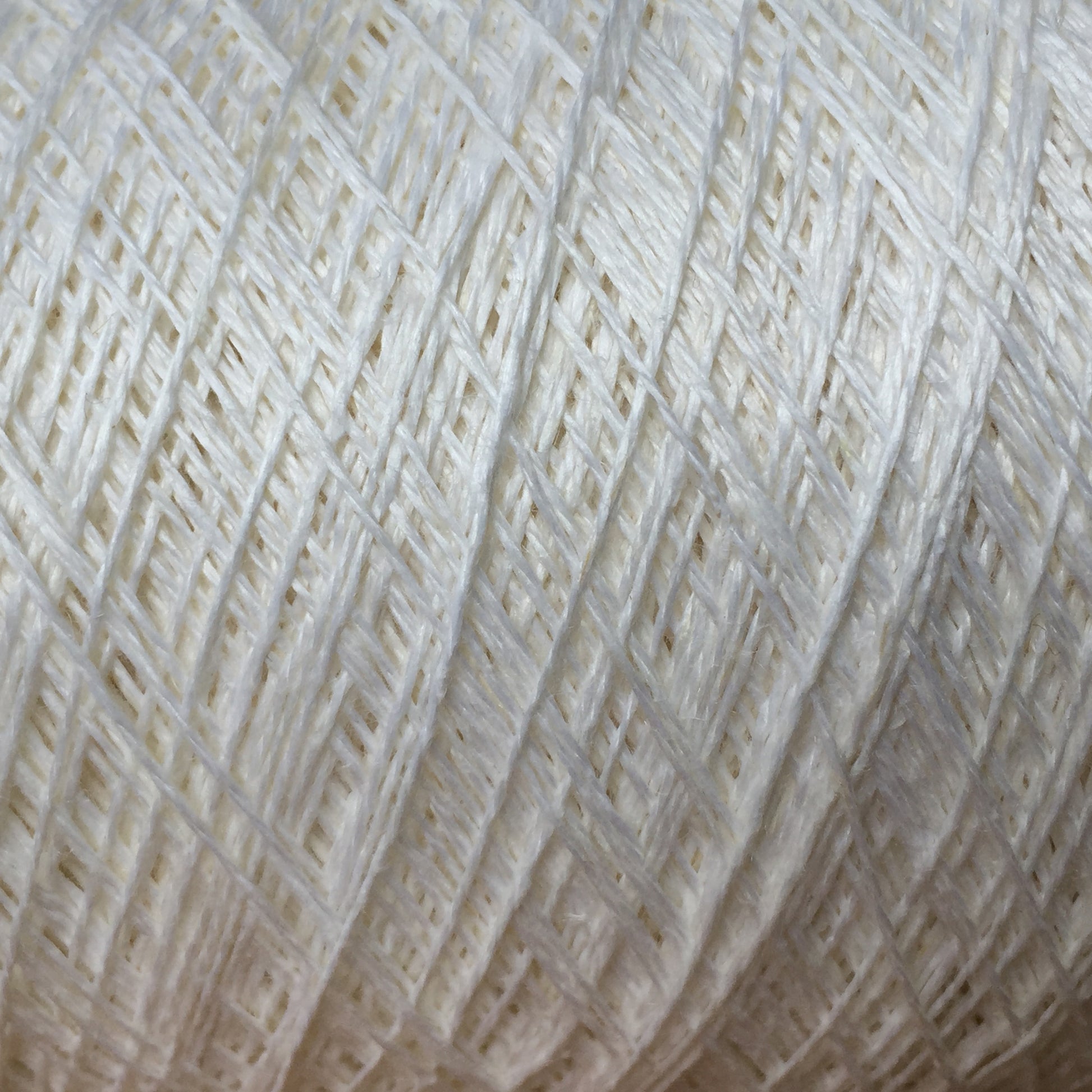 Close-up image of a ball of Newport 16/2 Linen Yarn | Mini-cone, showcasing its detailed texture and tightly wrapped strands. The Halcyon Yarn product appears soft and smooth, with crossing lines creating a crisscross pattern throughout.