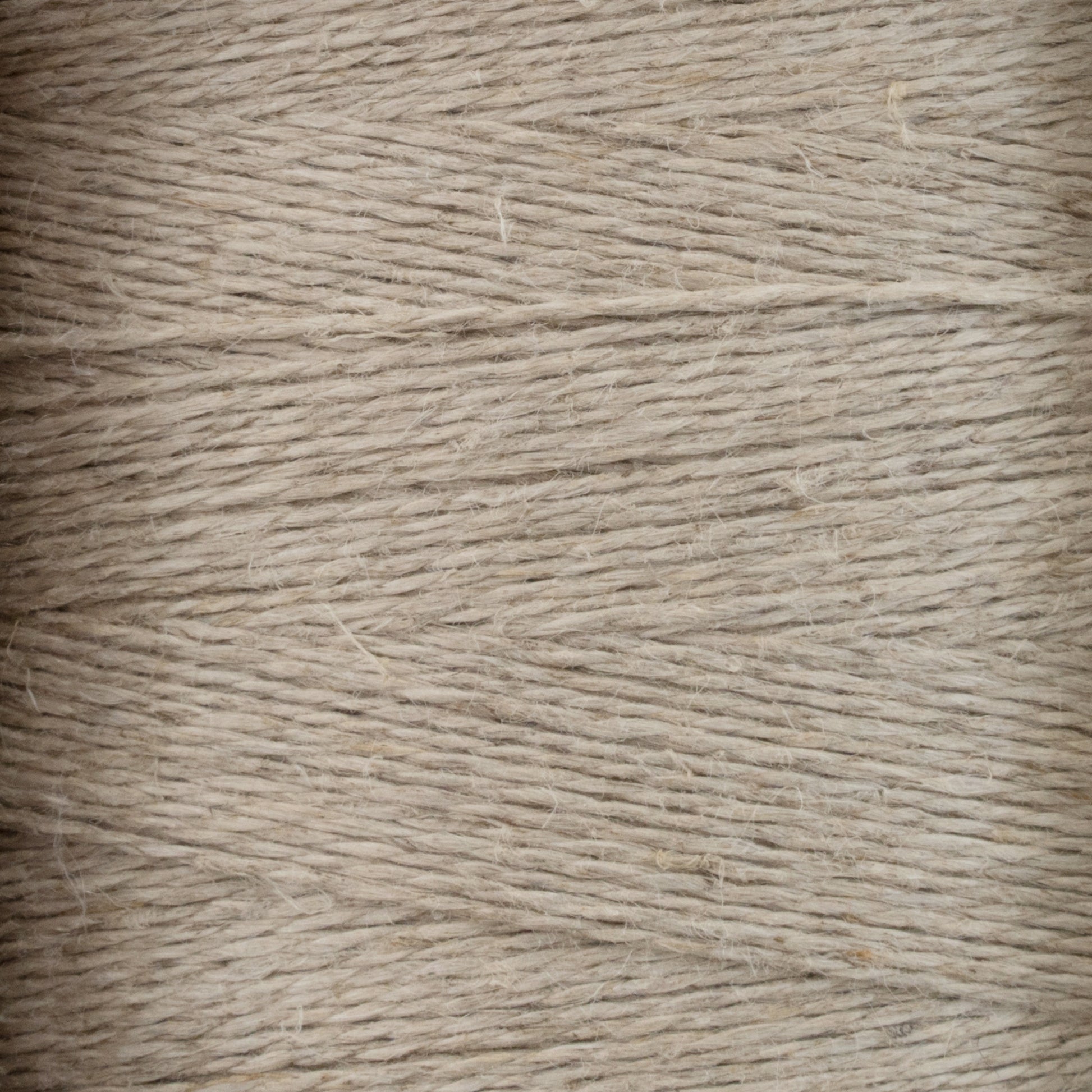 Close-up view of tightly wound beige Newport 16/2 Linen Yarn, showing the texture and fine fibrous strands. The yarn appears slightly rough, with varying thickness and a natural, rustic appearance reminiscent of woven items from Halcyon Yarn's collection.