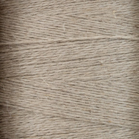 Close-up view of tightly wound beige Newport 16/2 Linen Yarn, showing the texture and fine fibrous strands. The yarn appears slightly rough, with varying thickness and a natural, rustic appearance reminiscent of woven items from Halcyon Yarn's collection.