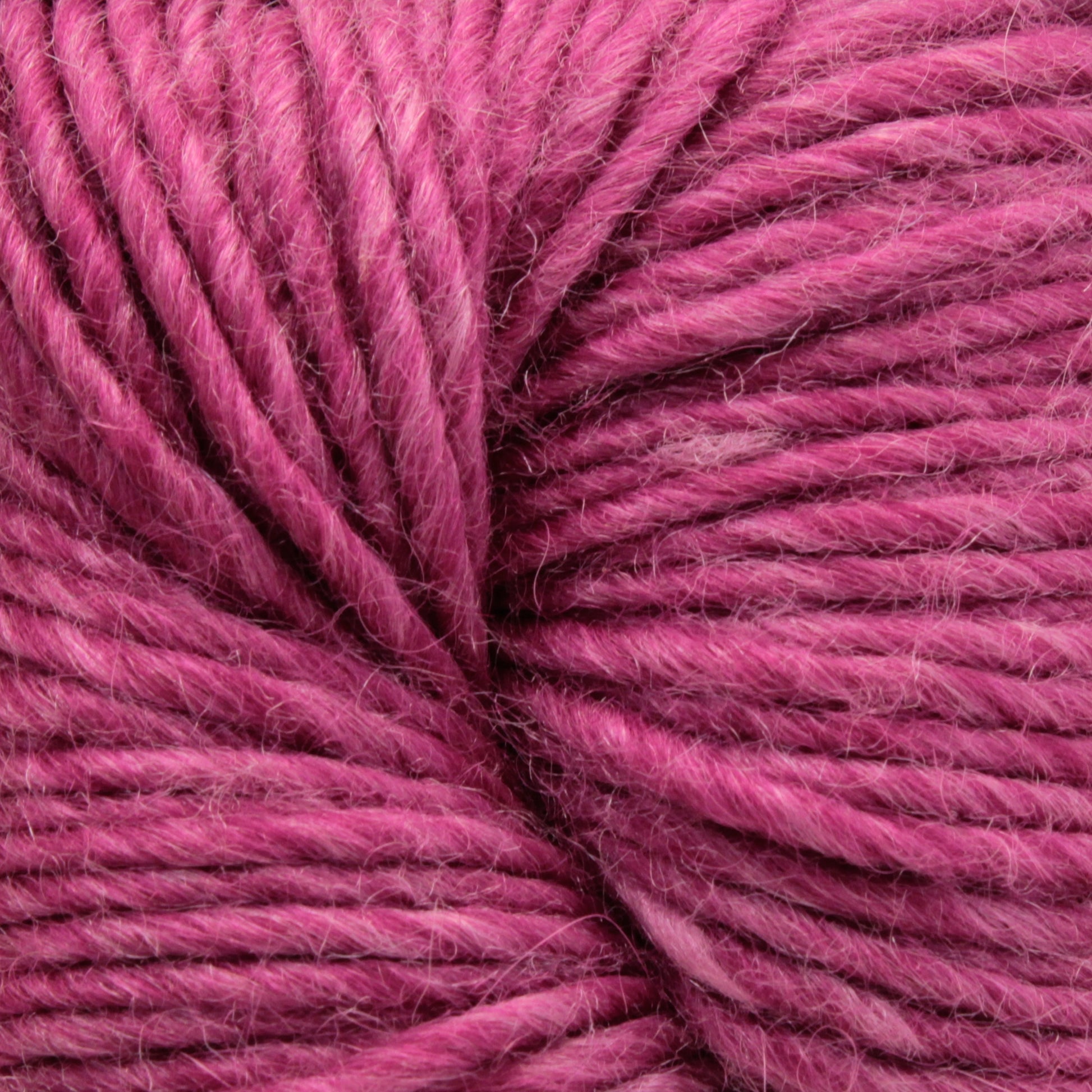 Close-up image of Moonshine by Juniper Moon Farm yarn, showing the detailed texture and intertwined fibers. The yarn, made from a luxurious blend of silk and alpaca, appears to be soft and slightly fuzzy, with a rich, vibrant pink color. This exquisite product is offered by the brand Knitting Fever / Euro.