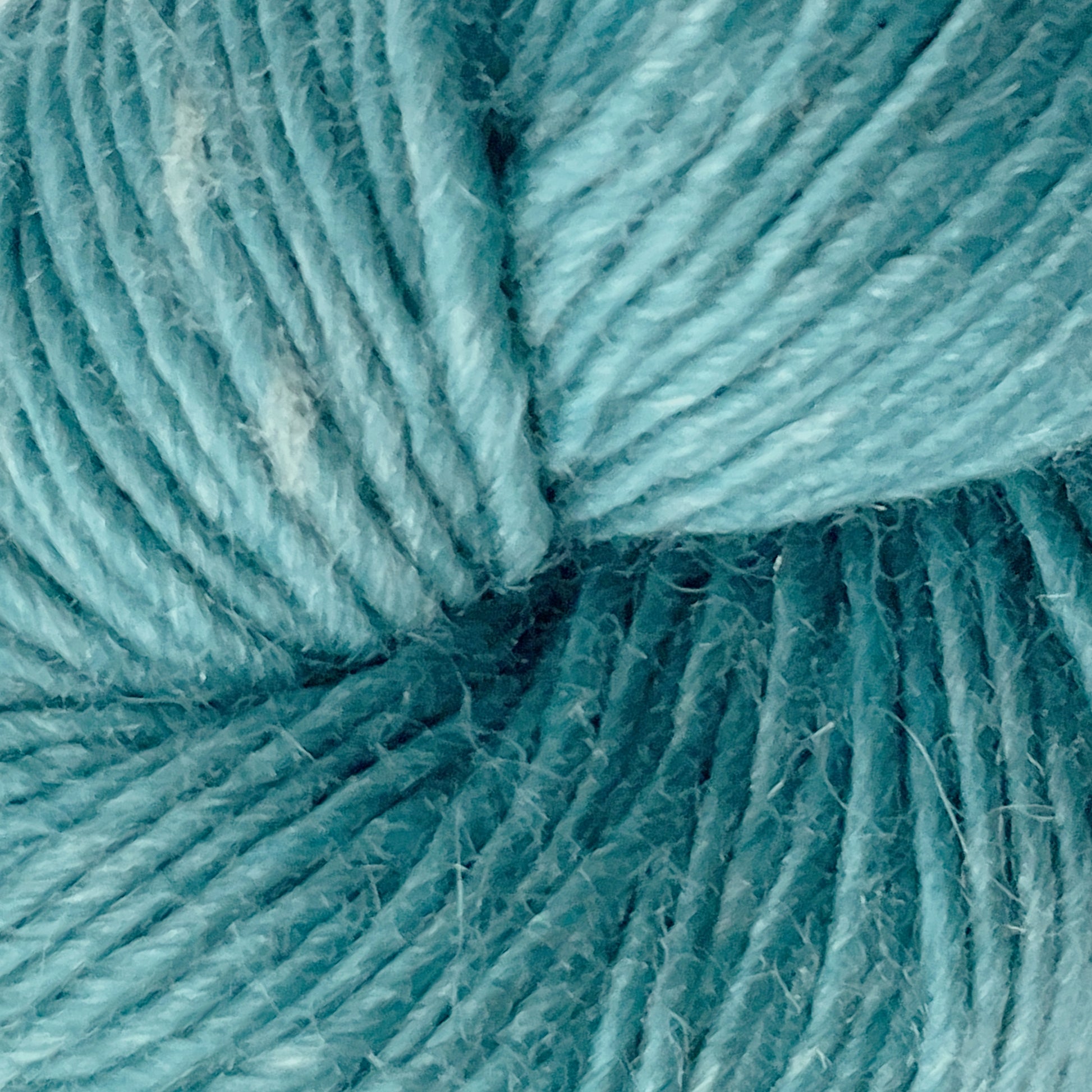 Close-up view of Moonshine by Juniper Moon Farm, a blue yarn tightly wound into a ball, displaying a soft and fluffy texture with small fibers visible. Made from alpaca wool by Knitting Fever / Euro, the yarn shows a gradient of light to medium blue tones, giving it a slightly variegated appearance.