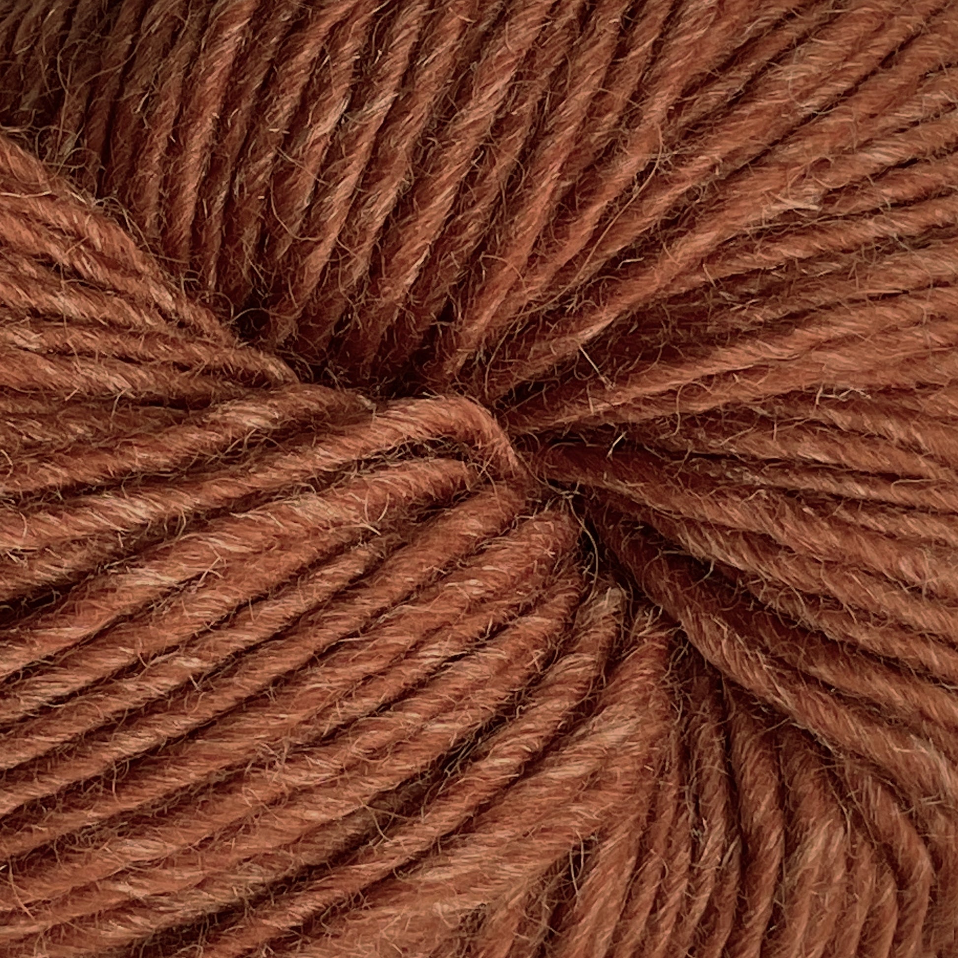 A close-up view of a ball of Moonshine by Juniper Moon Farm, showcasing tightly wound strands in a warm, earthy brown color. The texture appears slightly fuzzy, highlighting the soft and cozy quality of the alpaca wool material from Knitting Fever / Euro.