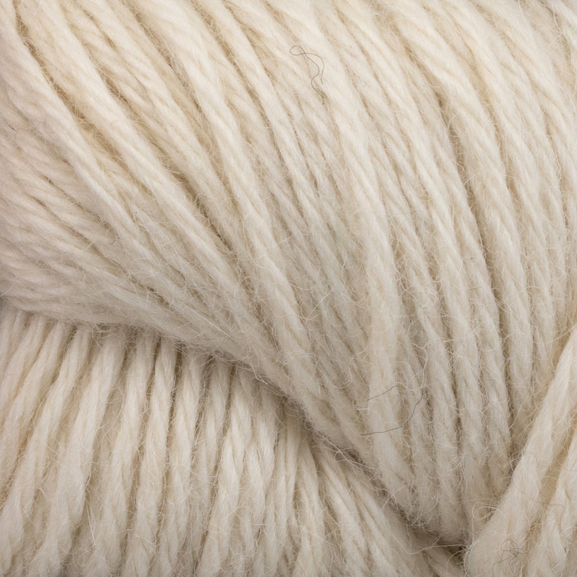 A close-up of a thick, cream-colored skein of Juniper Moon Farm Herriot Baby Alpaca from Knitting Fever / Euro. This DK weight yarn boasts a soft, fuzzy texture with strands that are slightly twisted together, creating a cozy and natural appearance.