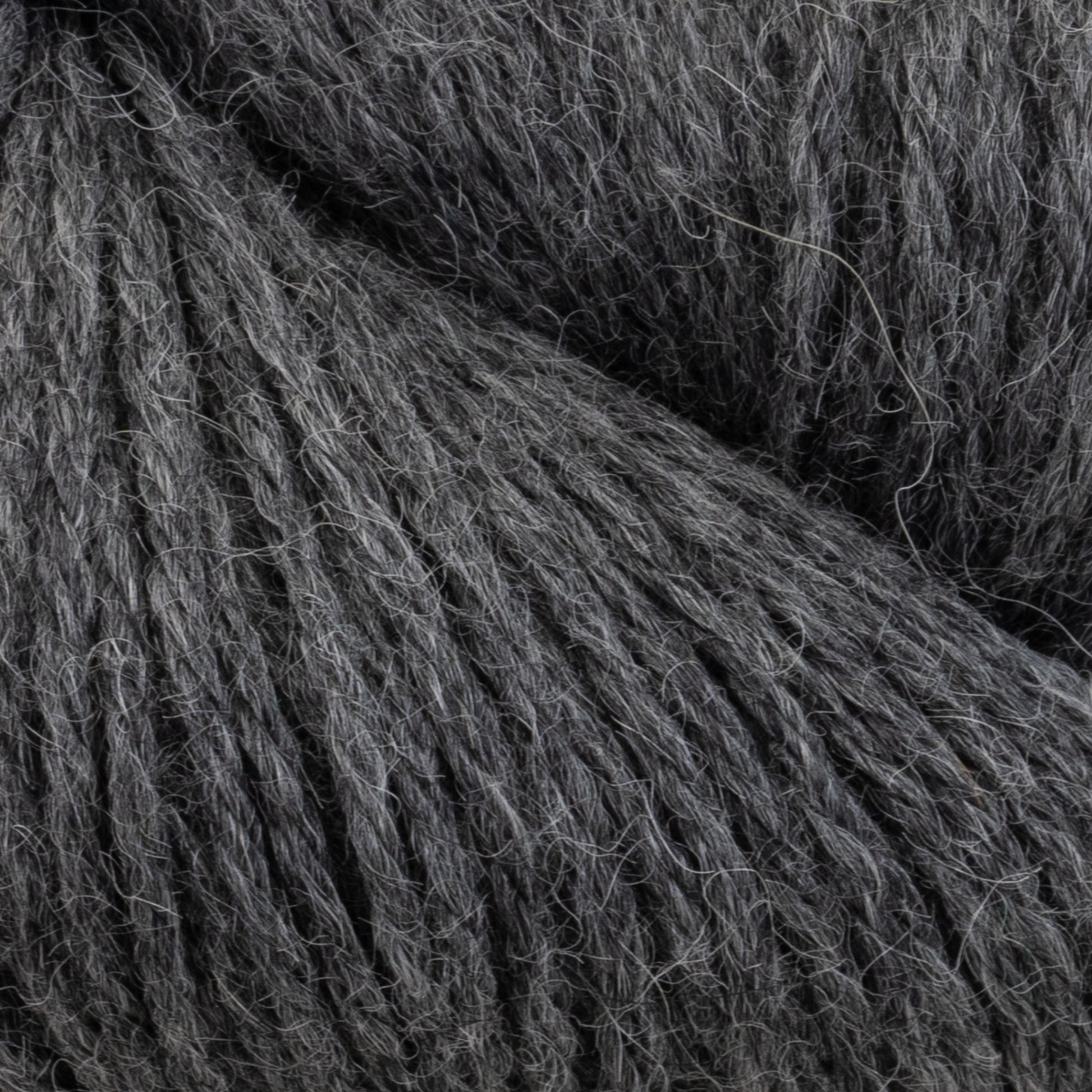 Close-up image of charcoal gray Juniper Moon Farm Herriot Baby Alpaca yarn from Knitting Fever / Euro showing fine fibers and soft texture. The DK weight yarn is densely packed, with individual strands visible, highlighting its thick and cozy appearance, suitable for knitting or crocheting projects.