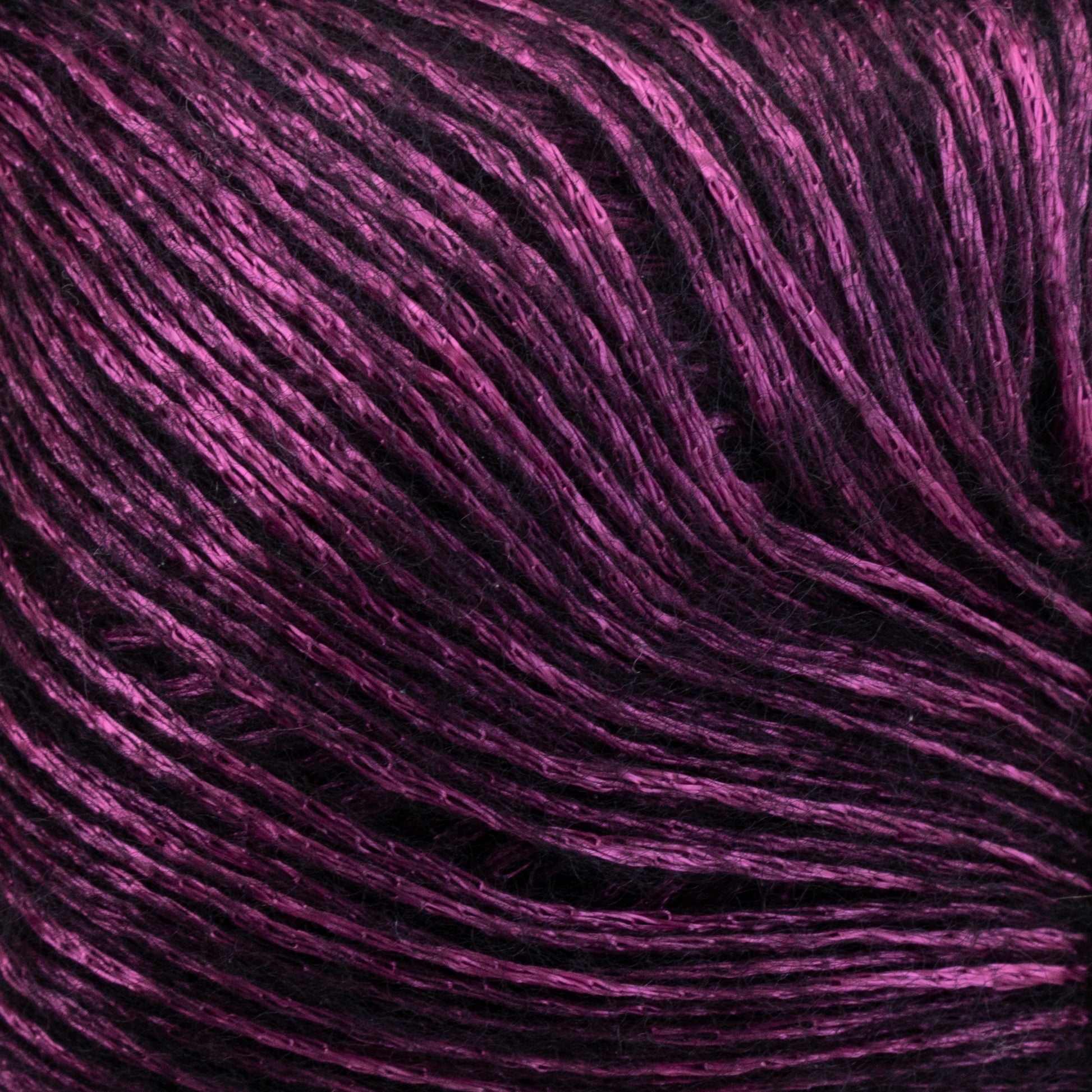 Close-up of a skein of Katia Air Lux yarn from Knitting Fever / Euro displaying a gradient of vibrant magenta and deep purple hues with a smooth, slightly glossy texture. The Merino wool strands are tightly wound together, showcasing the intricate pattern and depth of color.