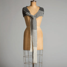 A dress form adorned in a Crescent Wrap by Yarn & Soul, elegantly draped around the shoulders and cascading down in front. The knit wrap transitions from dark to light gray towards the middle and bottom sections. The background is plain and neutral in color.