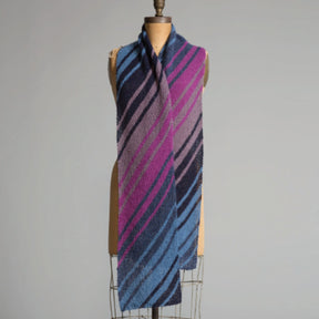 A long, knitted Diagonal Scarf with diagonal stripes in various shades of pink, purple, blue, and gray draped over a dress form against a plain background. Crafted with Superfine 400 Alpaca Braids by Yarn & Soul, the scarf appears soft and cozy, showcasing a gradient pattern. Enjoy this limited offer with a free pattern from Yarn & Soul!