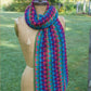 A colorful crocheted wrap, made with the Yarn & Soul pattern using Superfine 400 Alpaca, is draped around the neck of a vintage dress form mannequin. The wrap features a vibrant mix of hues in blue, green, pink, and purple. The scene is set outdoors with a grassy background and partial view of a wooden fence.