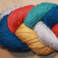 A close-up image of a twisted skein of Yarn & Soul's Superfine 400 Alpaca Braid yarn featuring various colors including teal, red, yellow, light gray, and blue. The sport weight yarn strands are neatly intertwined, showcasing their rich and vibrant hues against a neutral background.