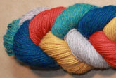 A close-up image of a twisted skein of Yarn & Soul's Superfine 400 Alpaca Braid yarn featuring various colors including teal, red, yellow, light gray, and blue. The sport weight yarn strands are neatly intertwined, showcasing their rich and vibrant hues against a neutral background.